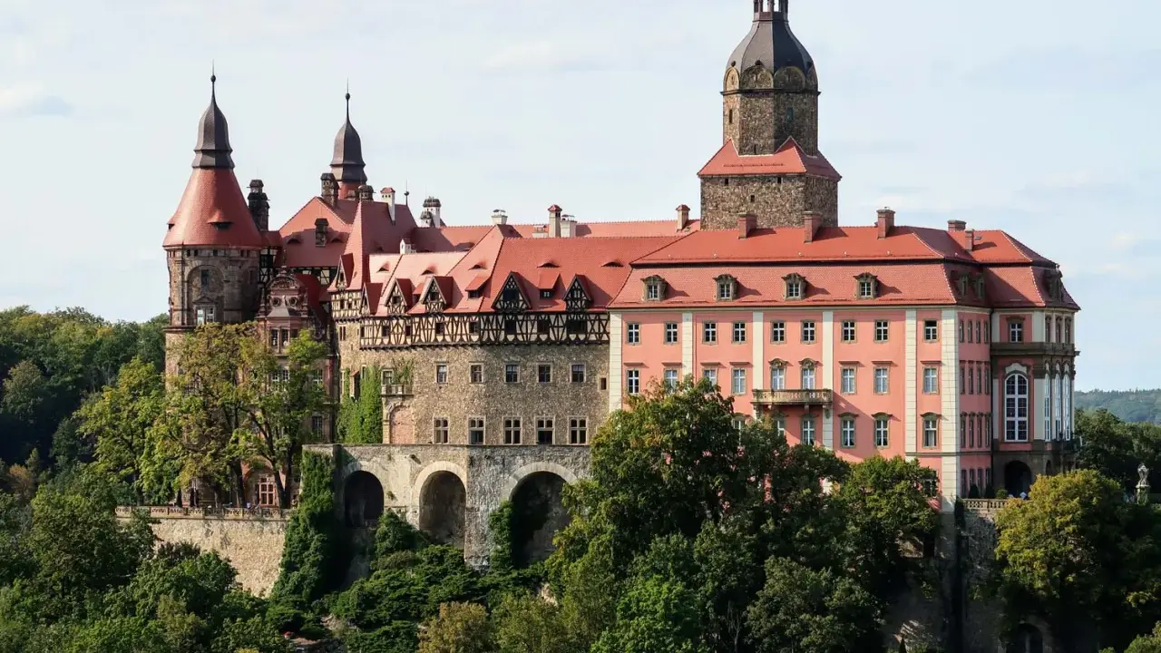 Zamek Książ z czerwonymi dachami i wieżami, otoczony zielenią. Sprawdź zamek książ cennik zwiedzania.