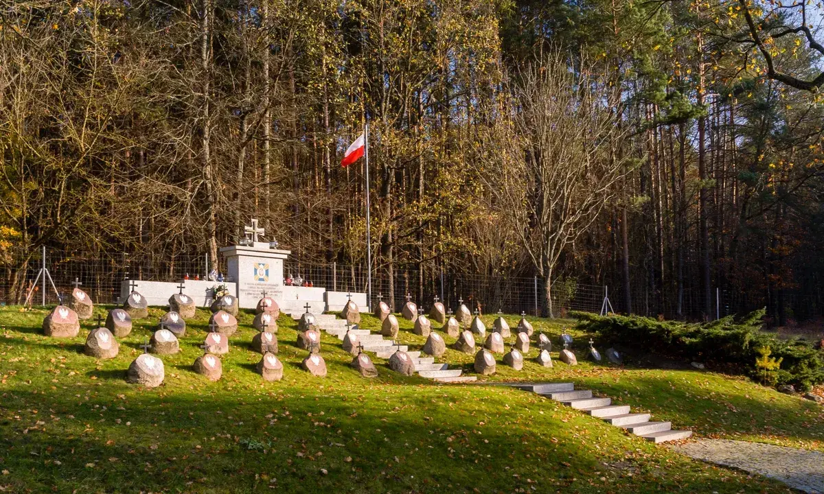 Cmentarz wojenny na kopnej górze, z rzędami kamiennych nagrobków i pomnikiem.