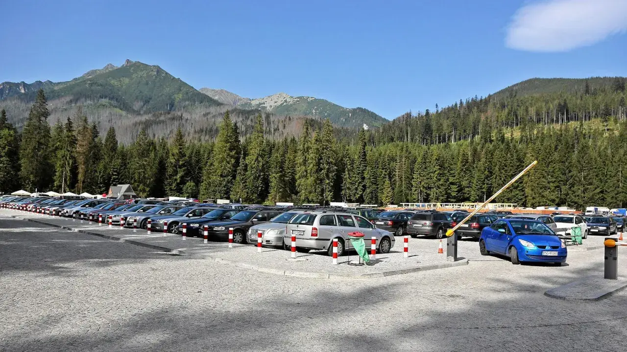Parking przed wejściem na Morskie Oko. Rząd samochodów pod górskimi szczytami i lasem.