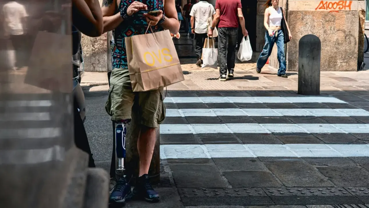 Mężczyzna z protezą nogi sprawdza telefon na ulicy w Barcelonie, obok przejścia dla pieszych. Ludzie spacerują, czy w barcelonie jest bezpiecznie?
