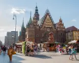 Tłum ludzi spaceruje po Rynku we Wrocławiu, podziwiając zabytkowy ratusz i letnie stoiska.