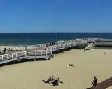 Słoneczny dzień na gdańskiej plaży Brzeźno. Ludzie spacerują po molo, odpoczywają na piasku, ciesząc się widokiem morza.