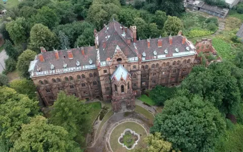 Mokrzeszów pałac, rozległy, ceglany budynek z charakterystycznym dachem, otoczony bujną zielenią.
