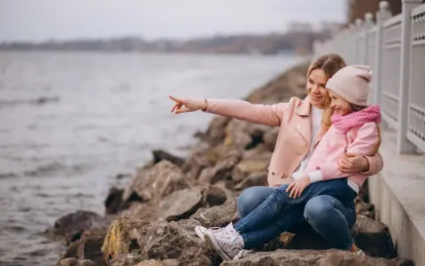 Mama z córką siedzą na kamieniach nad jeziorem. Mama wskazuje coś palcem, a dziewczynka się śmieje. To świetne gąski atrakcje dla dzieci.