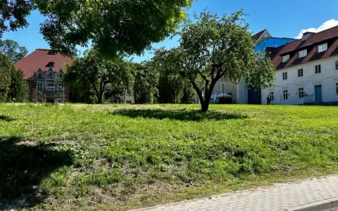 Zielona polana przed zabytkowymi budynkami, idealne miejsce na relaks i odkrywanie sztynort atrakcje.