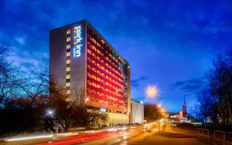 Wieczorem rozświetlony hotel Park Inn w Katowicach z kolorowym logo. Na ulicy widać światła samochodów.