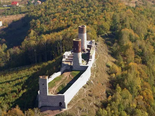 Ruiny zamku Chęciny na wzgórzu, otoczone jesiennym lasem. Sprawdź zamek Chęciny cennik przed wizytą.