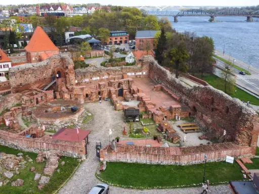Ruiny zamku bierzgłowskiego z czerwonej cegły, z widokiem na rzekę i most.