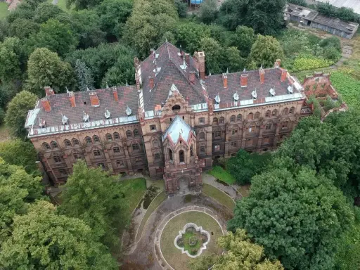Mokrzeszów pałac, rozległy, ceglany budynek z charakterystycznym dachem, otoczony bujną zielenią.