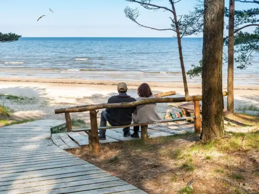 Para relaksująca para siedzi na ławce, patrząc na morze. Idealne miejsce na sanatoria nad morzem.