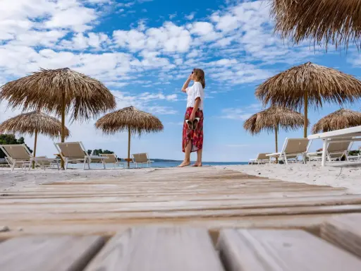 Kobieta na plaży, pod słomianymi parasolami, podziwia widok. To idealne miejsce na wyspie Rab, atrakcje czekają!