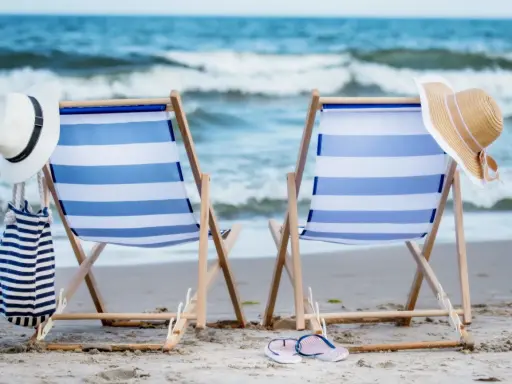 Dwa leżaki na plaży, gotowe na idealny weekend nad morzem. W tle szum fal i błękitne niebo.