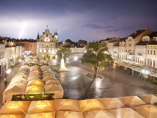 Nocny rzeszów rynek podczas burzy z piorunami. Mokry bruk, oświetlone kamienice i ogródki restauracyjne pod namiotami tworzą magiczny klimat.