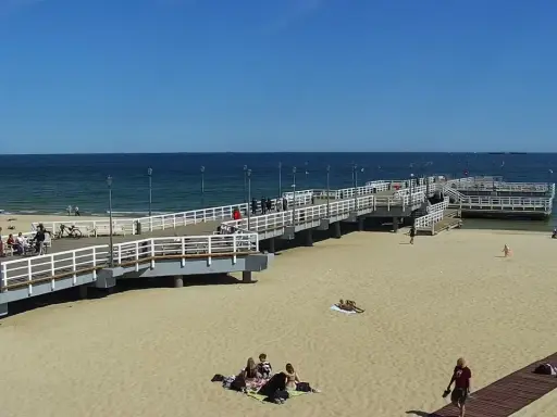 Słoneczny dzień na gdańskiej plaży Brzeźno. Ludzie spacerują po molo, odpoczywają na piasku, ciesząc się widokiem morza.