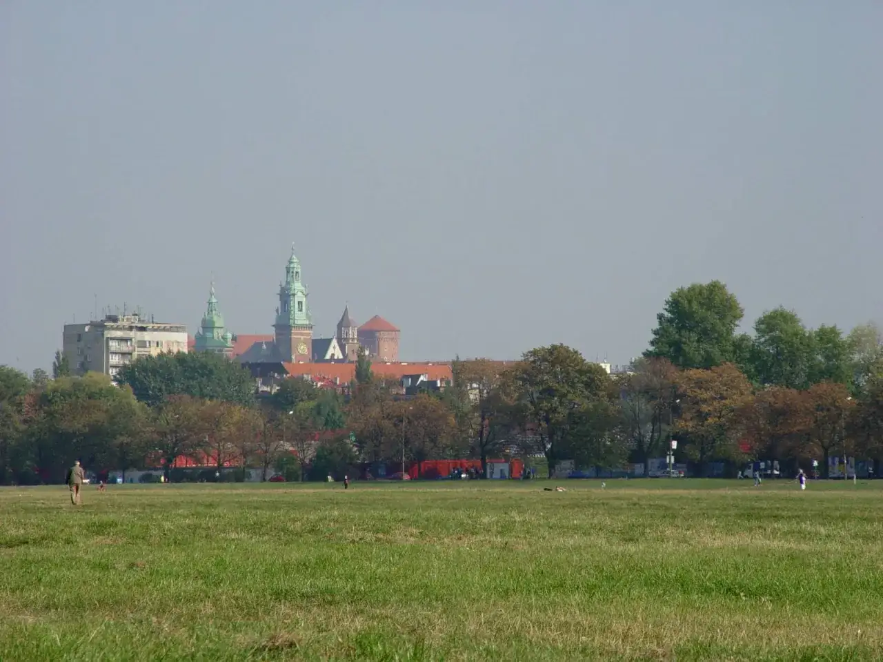 Spacer po błoniach krakowskich z widokiem na Wawel. Zieleń trawy i drzew kontrastuje z zabytkową architekturą.